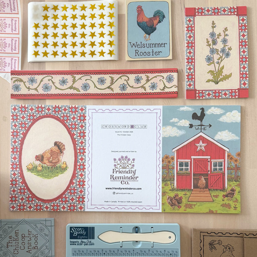 A flat lay of vintage-style craft or patterned paper items arranged on a light wood surface, including patterned cards, a rooster illustration card, a floral border strip, a chicken oval card, a recipe card, a barn scene card, and a small booklet or book page.